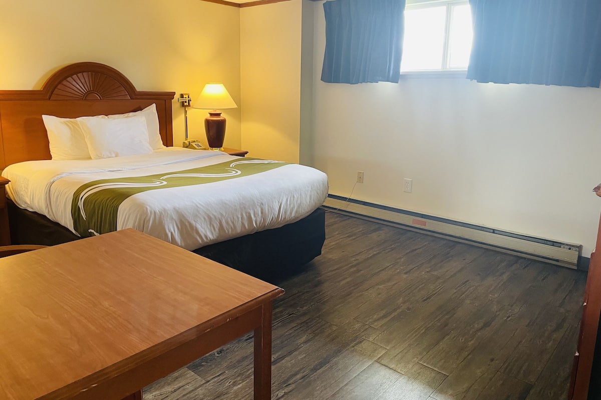 A hotel room with a bed, a bedside table, a lamp, and a window with curtains.