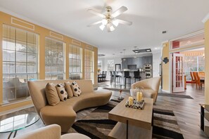A modern living room with a beige sofa, a glass coffee table, and a ceiling fan.