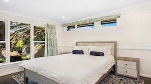 Relax in this serene bedroom with a large bed, two nightstands, and a large window offering a view of the surrounding greenery.
