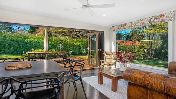 A modern living room with a dining area, large windows, and a view of a lush garden.