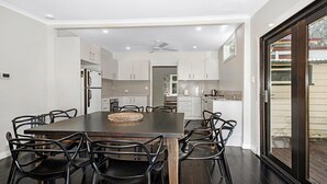 A modern kitchen with white cabinetry, a large dining table with black chairs, and a view through a glass door to the outside.