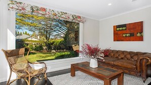 A living room with a large window, a wicker chair, a brown leather sofa, and a coffee table.
