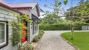 A house with a gravel driveway leading to a front door, surrounded by a well-maintained lawn and a hedge.