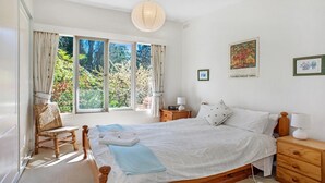 A bedroom with a large bed, a wooden nightstand, a chair, and a window with curtains. - Crabapple Southside Mountain Cottage Pet Friendly (WENTWORTH FALLS)