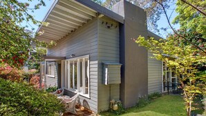 A single-story house with a porch, a chimney, and a small garden area with a table and chairs. - Crabapple Southside Mountain Cottage Pet Friendly (WENTWORTH FALLS)