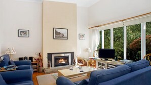A living room with a fireplace, blue sofas, a coffee table, and a television. - Crabapple Southside Mountain Cottage Pet Friendly (WENTWORTH FALLS)