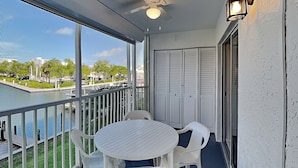 A balcony with a table and chairs, a view of a body of water, and a building in the background. - Royal Pelican 173 by Distinctive Beach Rentals (Fort Myers Beach)