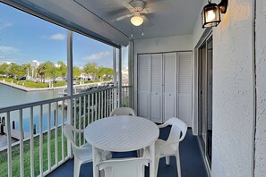 A balcony with a table and chairs, a view of a body of water, and a building in the background.