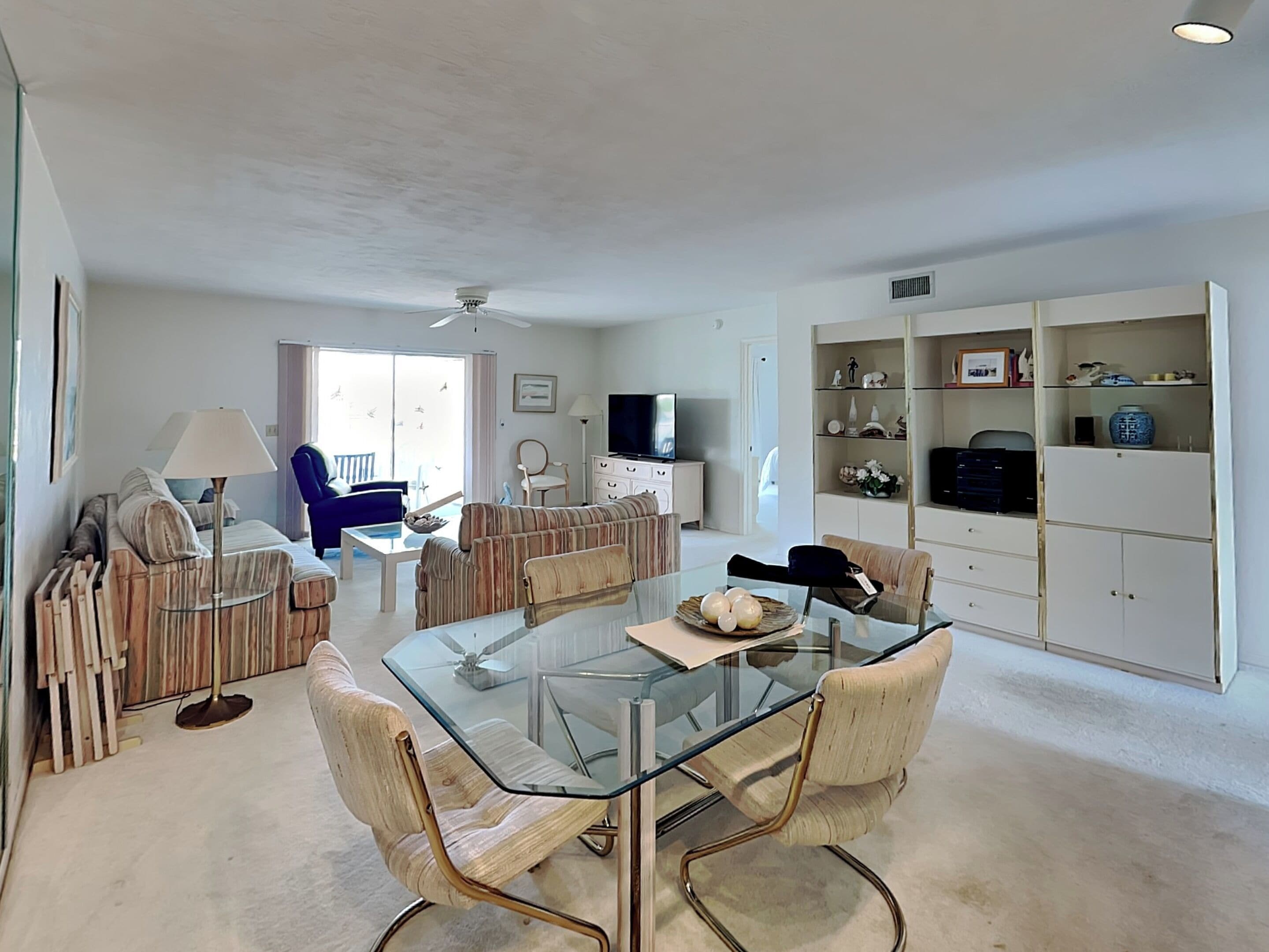 A modern living room with a glass-top dining table, sofas, a television, and a bookshelf.