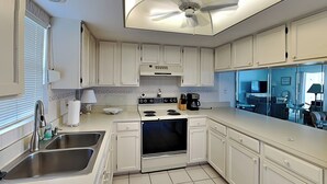 A modern kitchen with white cabinets, a built-in oven, a sink, and a ceiling fan. - Royal Pelican 173 by Distinctive Beach Rentals (Fort Myers Beach)