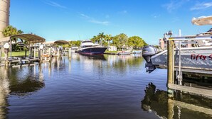 A marina with boats docked, a covered area with seating, and a clear blue sky. - Royal Pelican 173 by Distinctive Beach Rentals (Fort Myers Beach)