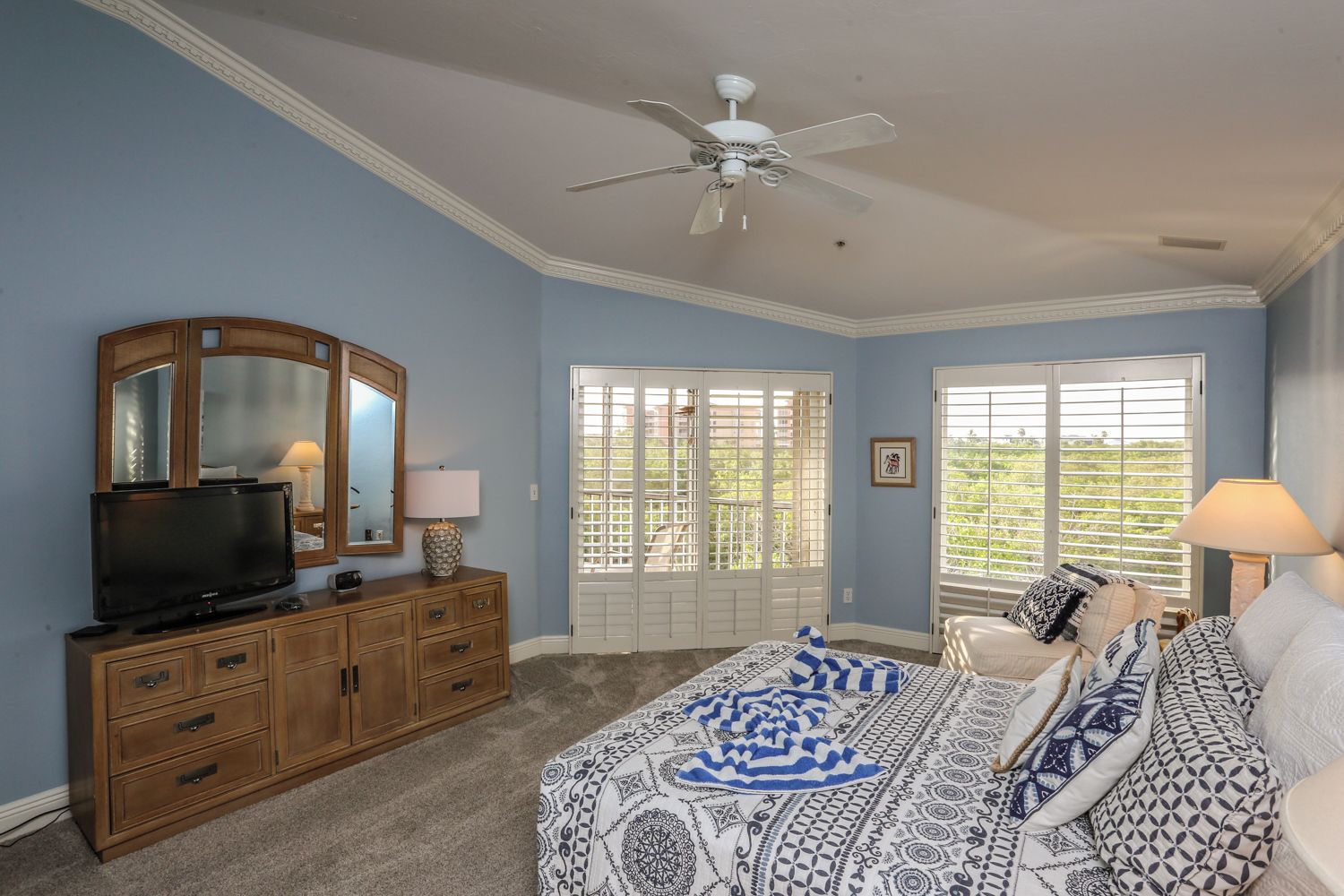 A bedroom with a bed, dresser, television, and a ceiling fan.