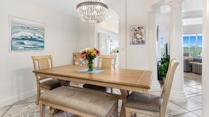 Un comedor con una mesa de madera, sillas con cojines, una araña y obras de arte en las paredes.