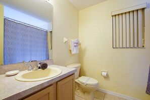 A bathroom with a sink, mirror, toilet, and a window with blinds.