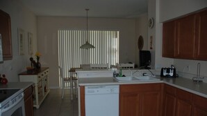 A kitchen with wooden cabinets, a dishwasher, a sink, and a dining area with a chair and table. - 4BR Davenport Pool Home by Watson-222CH (Davenport)