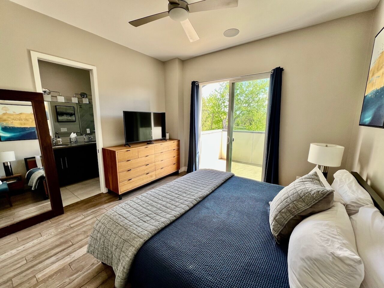 A bedroom with a bed, a dresser, a TV, and a balcony with curtains.