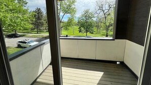 Een balkon met uitzicht op een groen park en een geparkeerde auto.