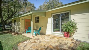 A small house with a porch, two chairs, a potted plant, and a stone patio.