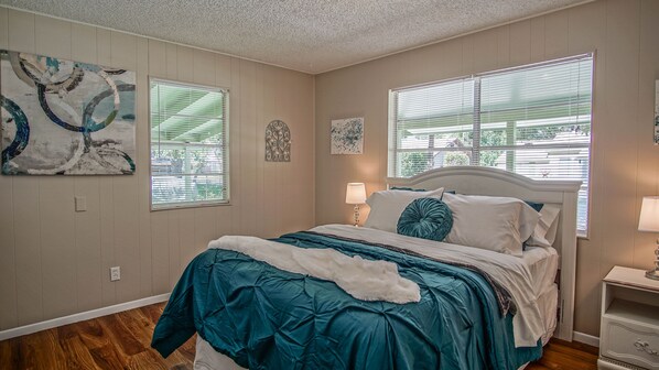 A bedroom with a bed, two bedside tables, a nightstand, and a window with blinds.