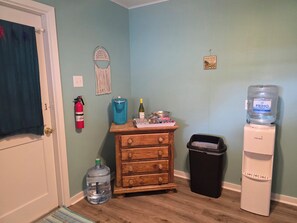 A room with a wooden dresser, a water dispenser, a trash bin, a fire extinguisher, and a water jug.