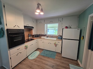 Eine Küche mit weißen Schränken, einem schwarzen Backofen, einer Mikrowelle, einem Spülbecken und einem Kühlschrank.