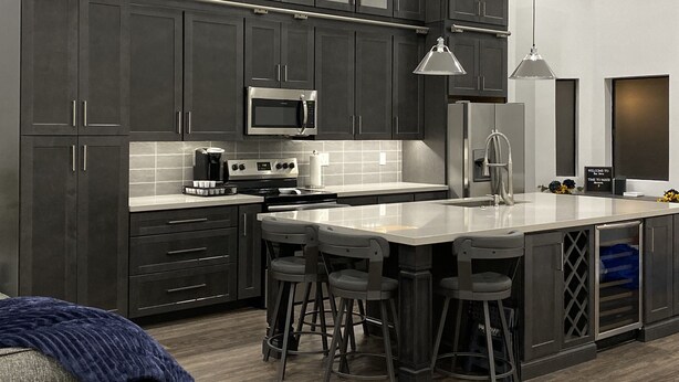 A modern kitchen with dark cabinets, stainless steel appliances, a central island with bar stools, and a welcoming sign. - Upscale Fully Renovated Biltmore Penthouse (Phoenix)