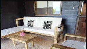 A room with a sofa, two wooden tables, and a bench. - Tupuna Lodge Apartments (Hanga Roa)