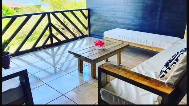 A balcony with a wooden table and a sofa, a potted plant, and a view of the sea. - Tupuna Lodge Apartments (Hanga Roa)