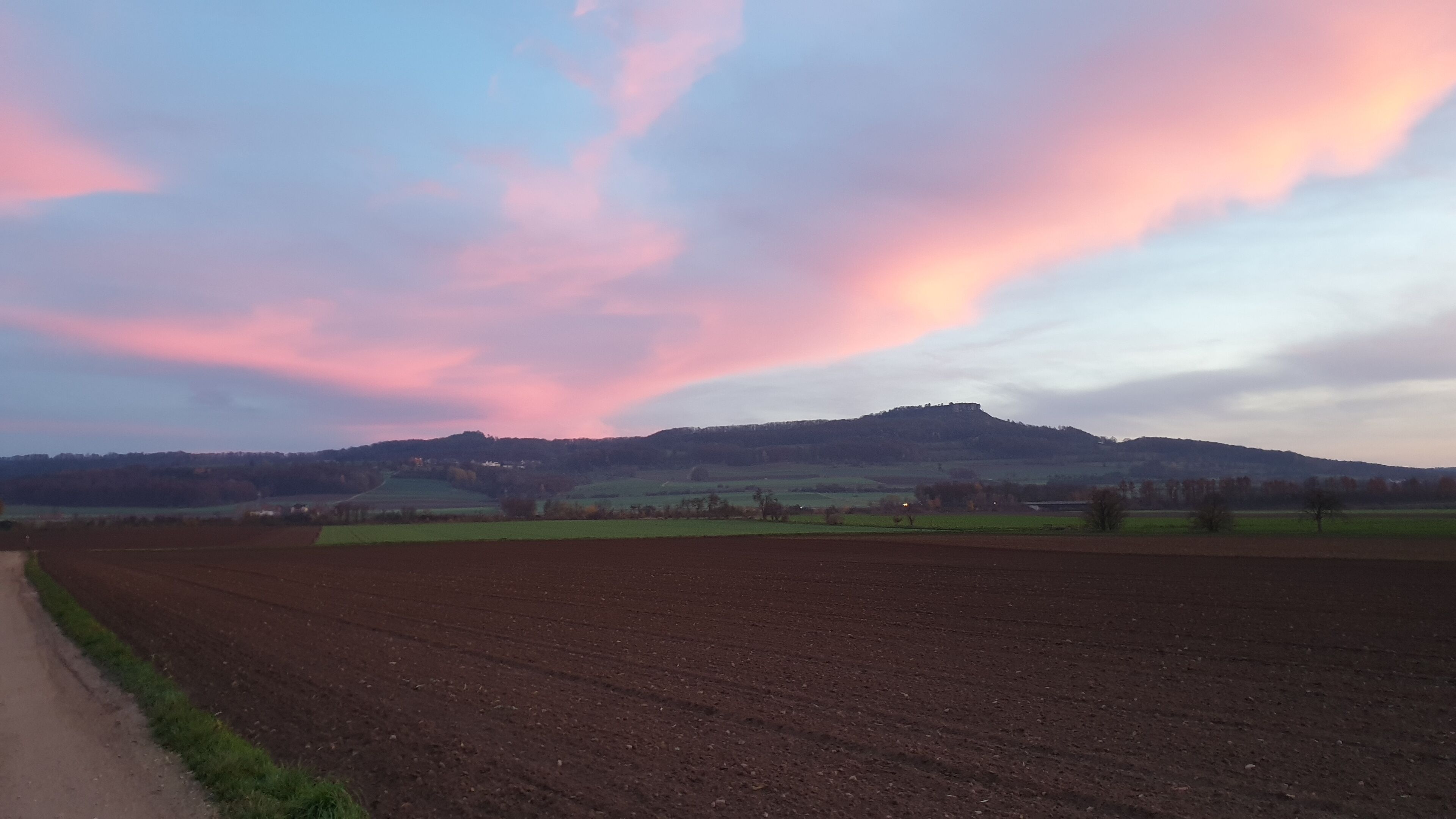 Paisagem rural com um campo arado e uma colina ao fundo.