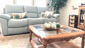 A living room with a light blue sofa, a wooden coffee table, a large green plant, and a wooden cabinet with a bird sculpture.