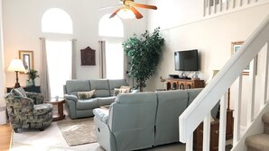 A spacious living room with a grey sofa set, a patterned armchair, a television, and a staircase.