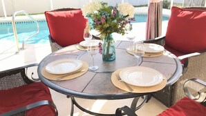A round table with a vase of flowers, set for four with plates, cutlery, and glasses.