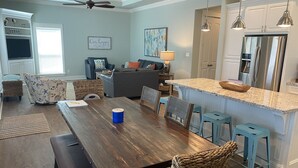 A modern kitchen with a central island, a dining area with a wooden table and wicker chairs, and a living room with a sofa and a ceiling fan. - Feelin’ Tip Sea - *Sleeps 10* Walking Distance to the beach! (Crystal Beach)