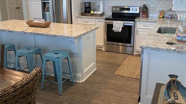 A modern kitchen with white cabinetry, stainless steel appliances, and a central island with stools. - Feelin’ Tip Sea - *Sleeps 10* Walking Distance to the beach! (Crystal Beach)
