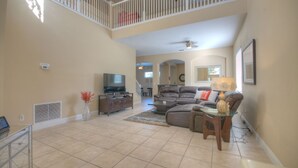 A spacious living room with a high ceiling, a large sectional sofa, a glass coffee table, and a television. - 4BR Davenport Pool Home by Watson-767OX (Davenport)