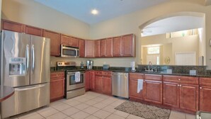 A modern kitchen with stainless steel appliances, wooden cabinets, and a granite countertop. - 4BR Davenport Pool Home by Watson-767OX (Davenport)