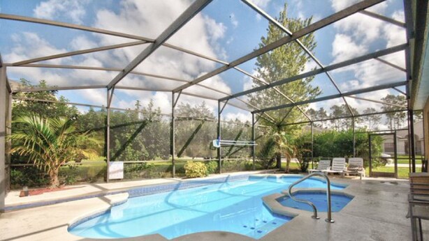 A covered outdoor swimming pool with a metal frame, surrounded by greenery and trees. - 4BR Davenport Pool Home by Watson-767OX (Davenport)