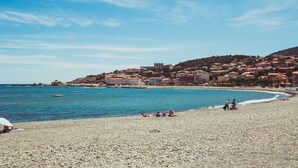 En strand med småsten och byggnader i bakgrunden.