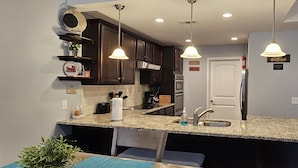A kitchen with granite countertops, dark wooden cabinets, stainless steel appliances, and pendant lighting.