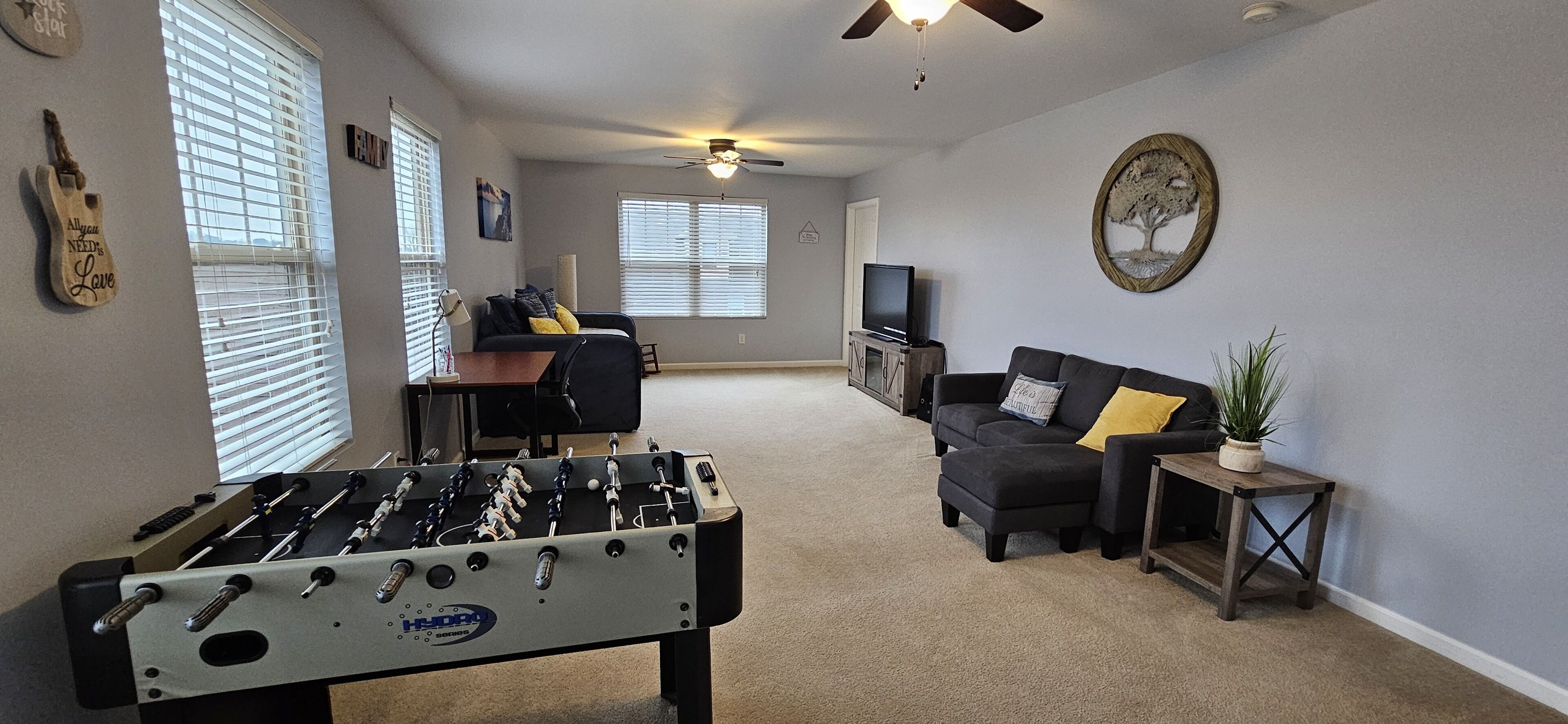 A living room with a foosball table, a sofa, a TV, and a ceiling fan.