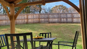 A covered patio with a table and chairs, a wooden fence in the background, and a clear sky.