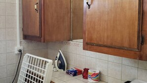 Une cuisine avec des meubles de rangement en bois, un radiateur blanc, un fer à repasser et quelques produits de nettoyage.