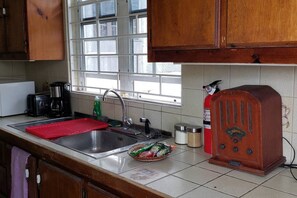 A kitchen with wooden cabinets, a window, a sink, a coffee maker, a radio, and a red mat.