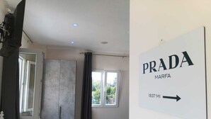 Una habitación con un armario, una silla azul, un televisor y un cartel que indica 'PRADA MARFA 1837 MI'.