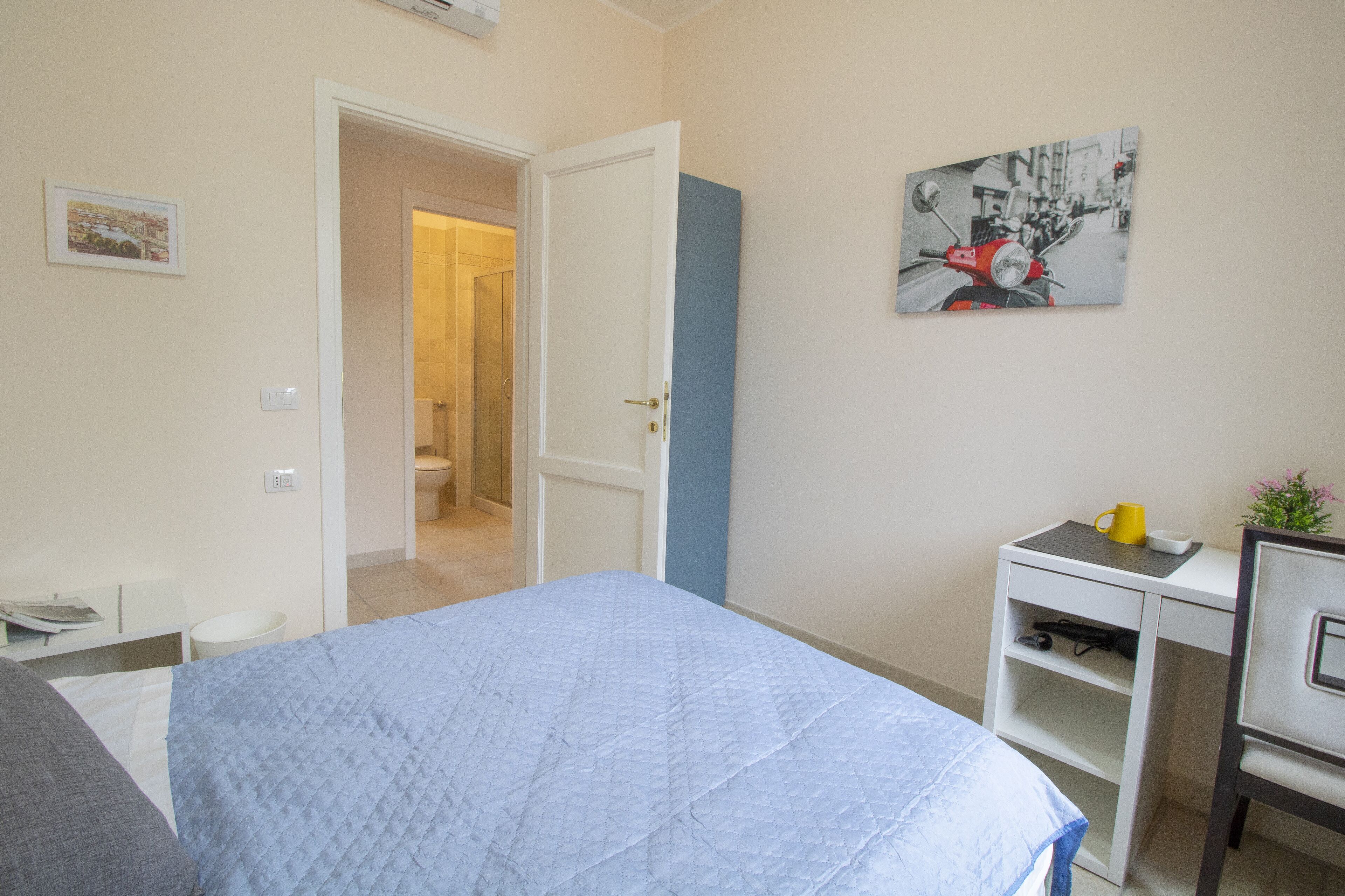 A bedroom with a bed, a desk, and a chair. There is a door leading to a bathroom.
