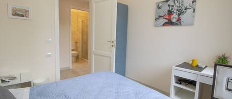 A bedroom with a bed, a desk, and a chair. There is a door leading to a bathroom.