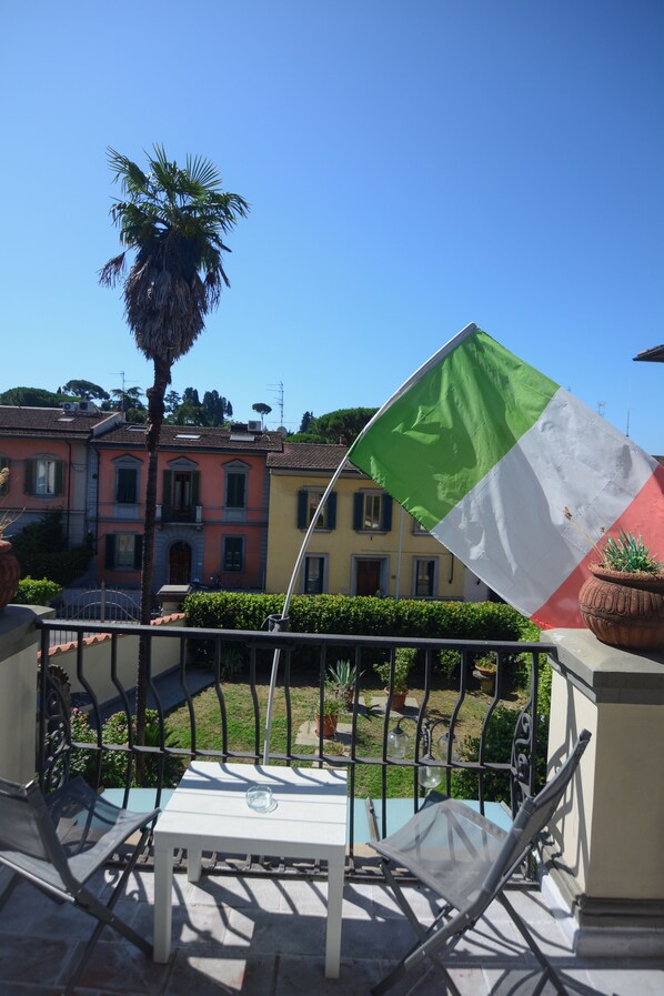 A balcony with a table and chairs, a flag, and a palm tree. - Villa Gelsomino Garden (Florence)
