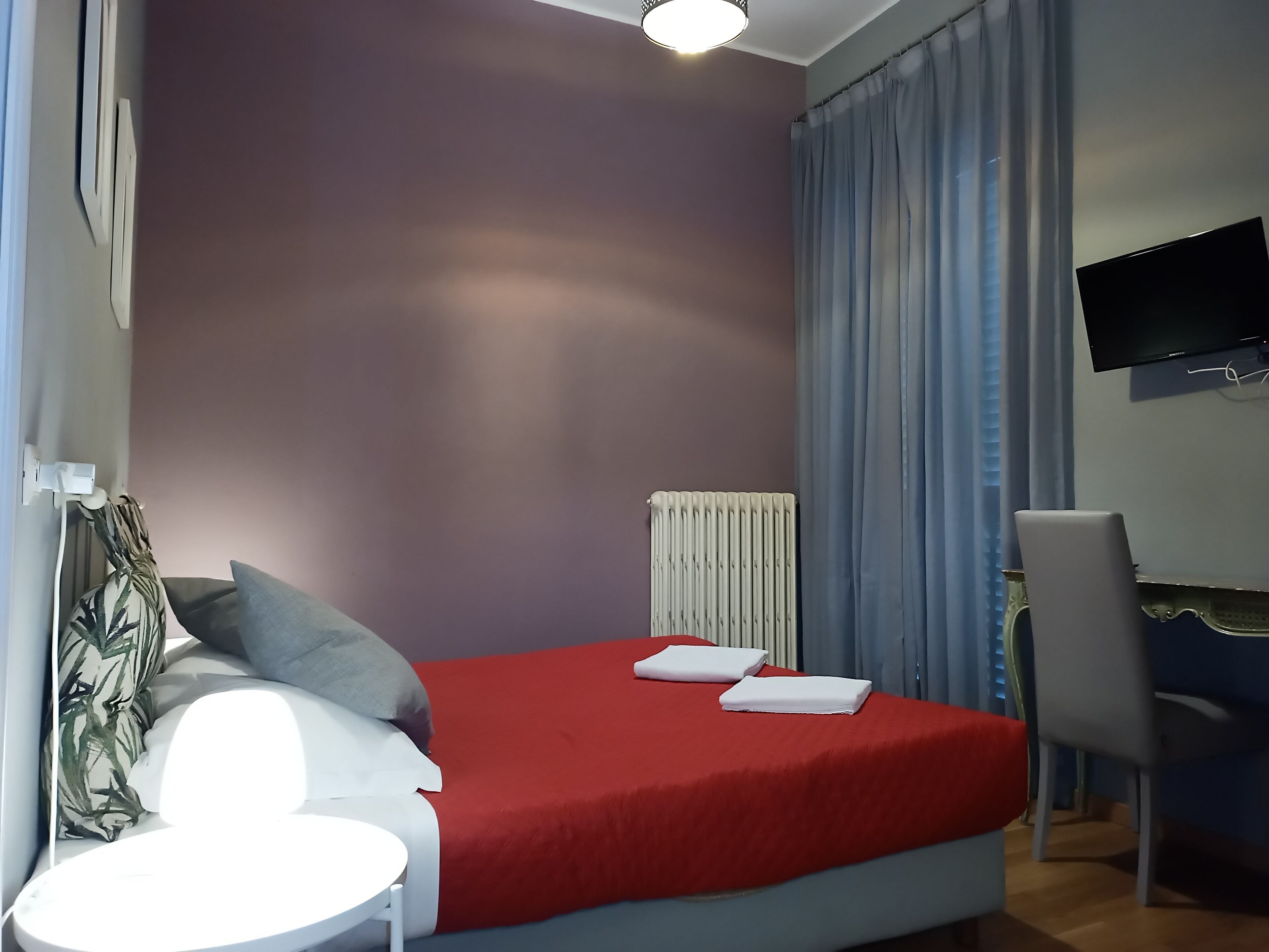 Habitación de hotel con cama, escritorio, silla, televisor y radiador.