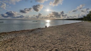 Una playa con un mar tranquilo, cielo despejado y algunas embarcaciones.