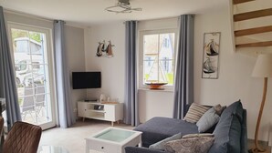 Una sala moderna con sofá, mesa de centro, televisor y ventana con cortinas.
